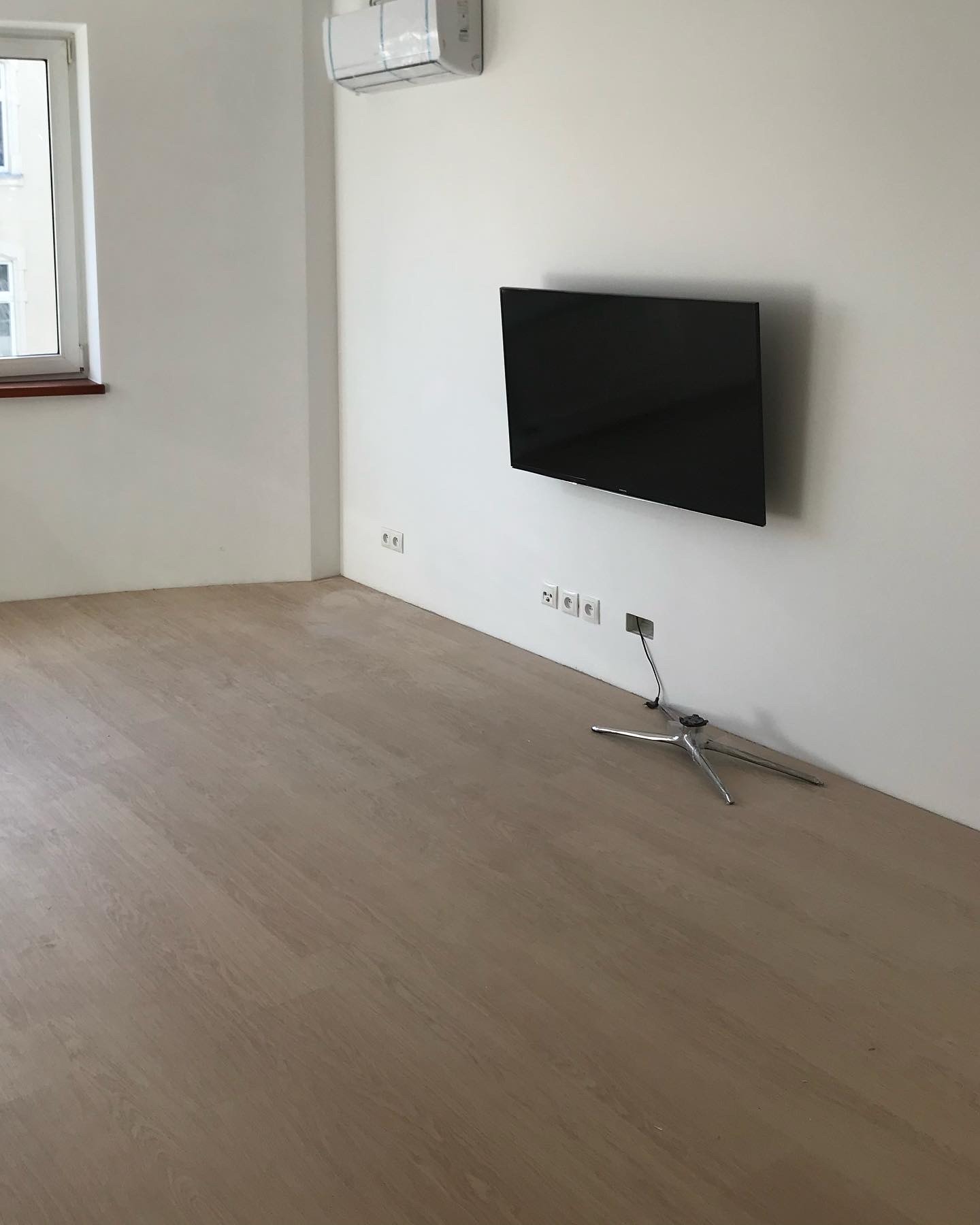 Wnętrze pokoju po montażu klimatyzacji i telewizora: klimatyzator na ścianie pod sufitem, telewizor na ścianie z wystającym kablem, jasna podłoga.