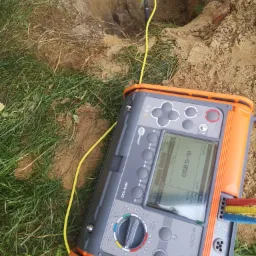 Pomiar uziemienia za pomocą miernika Sonel MPI-520 na trawie obok wykopu z wbitym prętem uziemiającym.