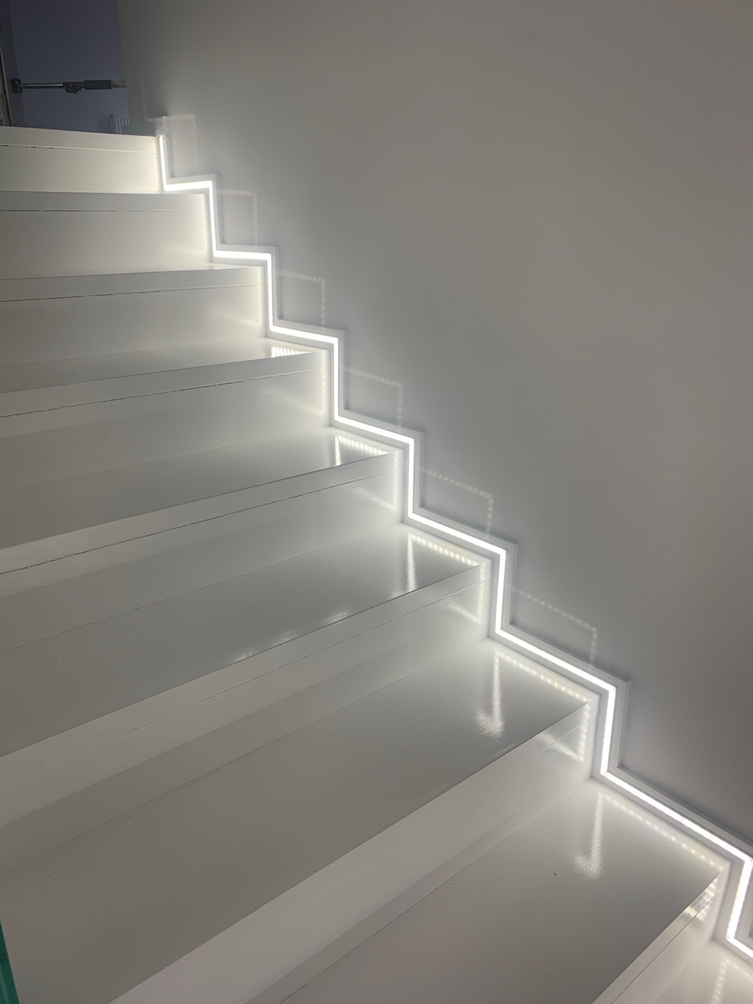 Białe schody z podświetleniem LED wzdłuż krawędzi stopni, oświetlające ścianę.