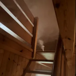 Wnętrze drewnianego domu z widocznymi schodami i unoszącą się parą, prawdopodobnie po zabiegu osuszania.
