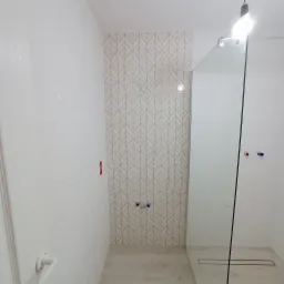 Wykończona łazienka z kabiną prysznicową typu walk-in, białe płytki z delikatnym wzorem liści na jednej ścianie, widoczne przyłącza wodne i odpływ liniowy.