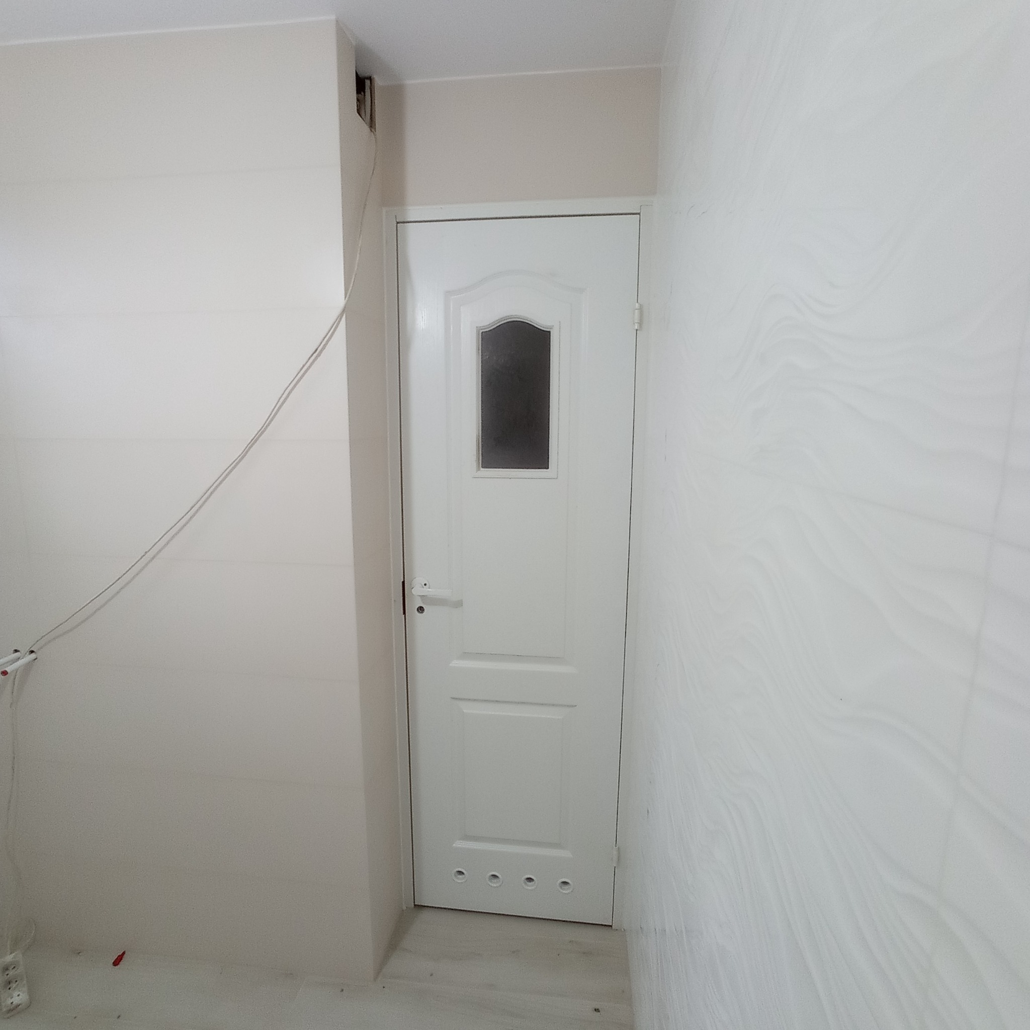 Białe drzwi z szybką wstawione w świeżo wyremontowanym pomieszczeniu z białymi płytkami na ścianach i podłodze, widoczne otwory wentylacyjne w dolnej części drzwi.