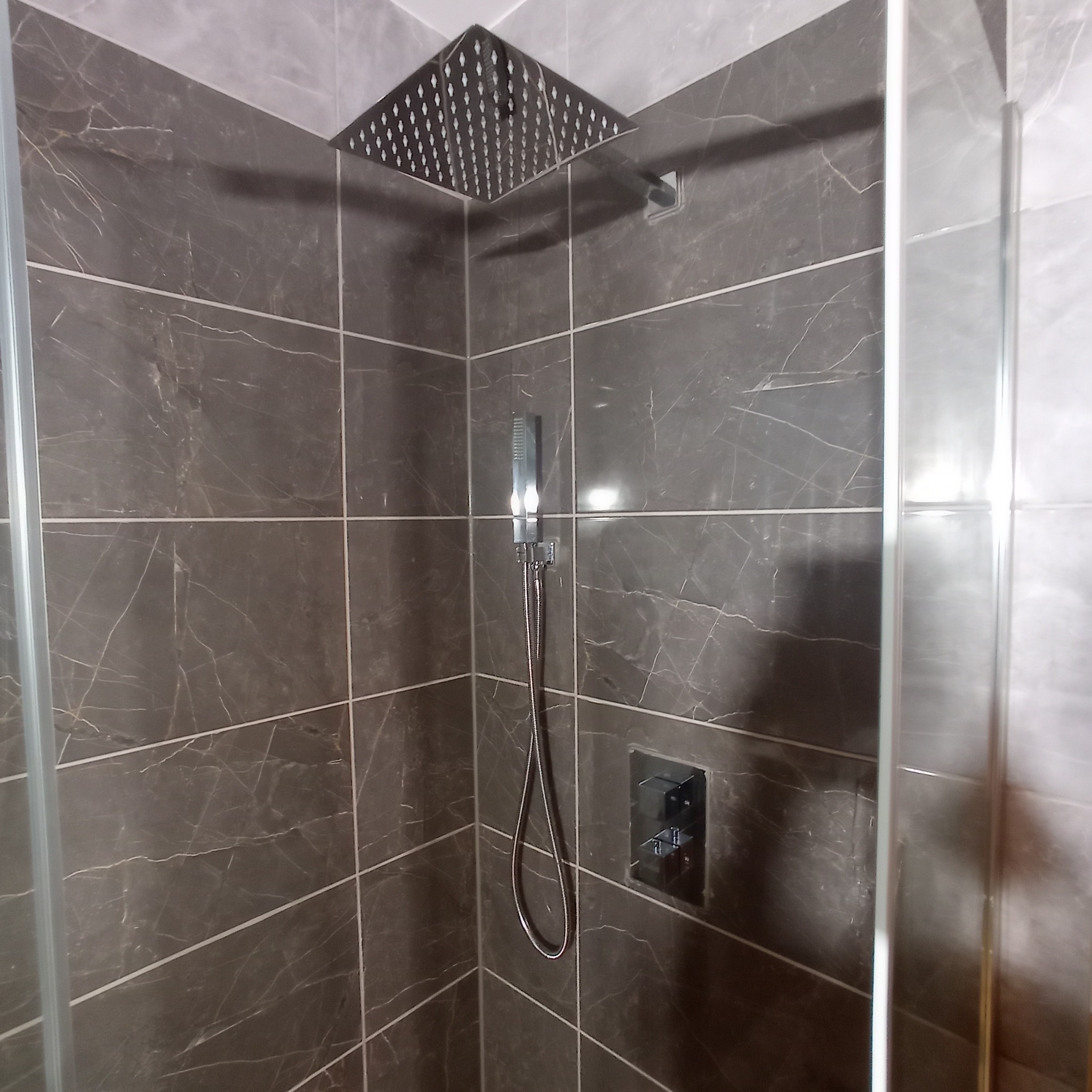 Nowoczesna kabina prysznicowa z deszczownicą i termostatem, wykończona szarymi płytkami imitującymi marmur z wyraźnym rysunkiem żyłkowania.