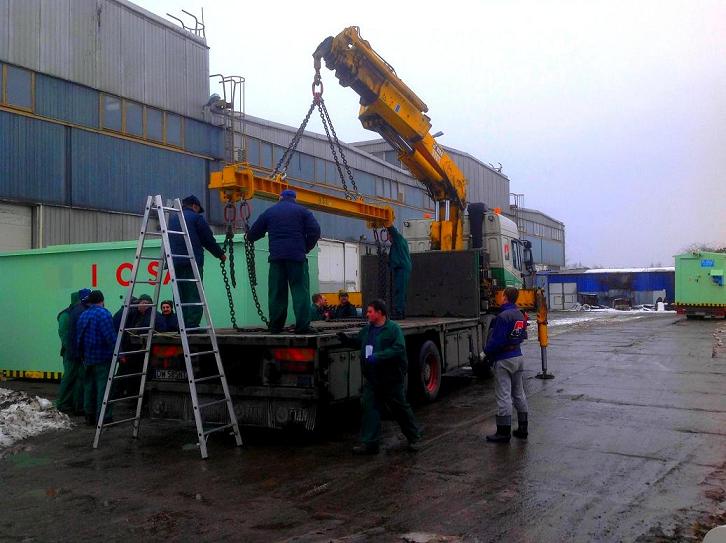 Załadunek zielonego kontenera z napisem 'ICS' na platformę ciężarówki za pomocą dźwigu HDS; pracownicy w odzieży roboczej nadzorują operację, drabina oparta o kontener.