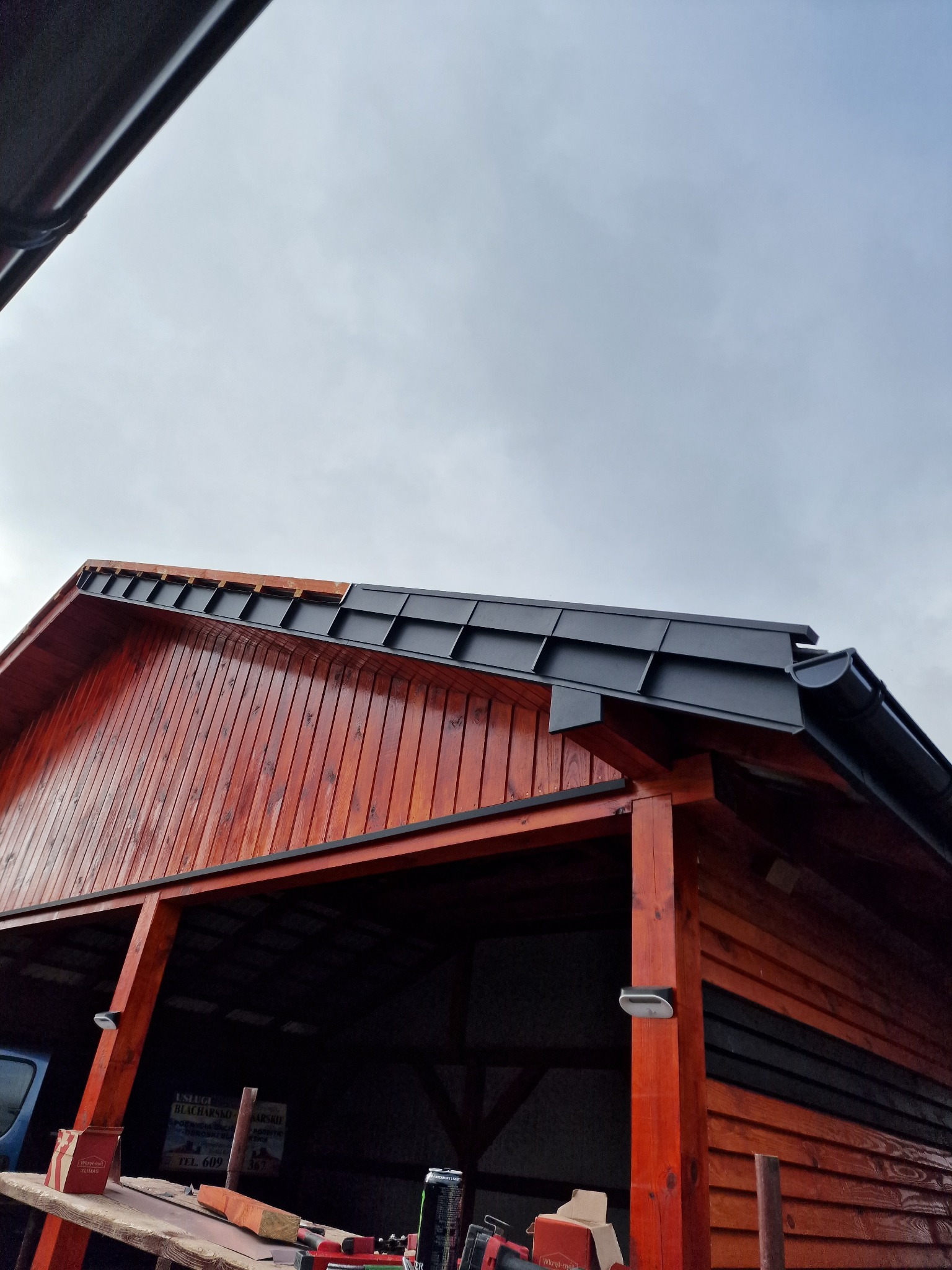 Nowy, czarny dach z blachy na drewnianej konstrukcji, z zamontowaną rynną, widziany z dołu pod kątem, z widocznym fragmentem nieba.