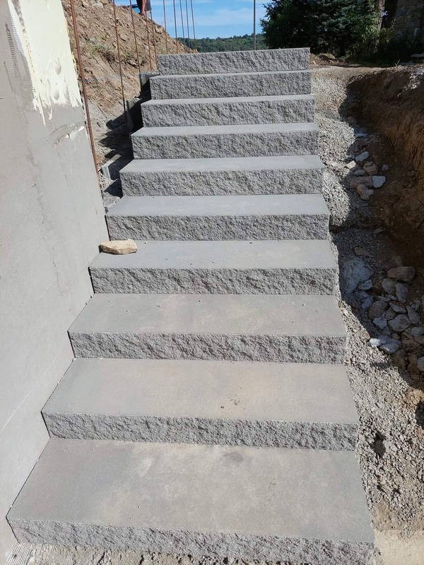 Granitowe schody zewnętrzne w Jaworzu, prowadzące w górę zbocza. Solidne, szare stopnie z surowym wykończeniem, osadzone w ziemi. Widoczne prace ziemne w tle.