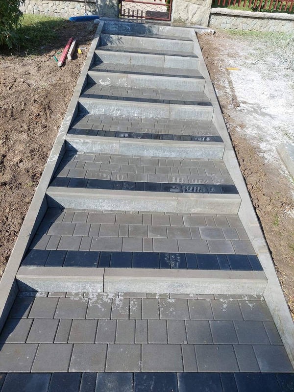 Schody z kostki brukowej w odcieniach szarości i czerni, prowadzące do furtki. Widoczne precyzyjne ułożenie i estetyczne wykończenie.