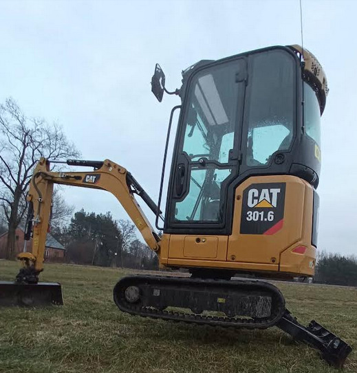 Żółta maszyna budowlana CAT 301.6, widok z boku na trawiastym terenie, antena na dachu kabiny.
