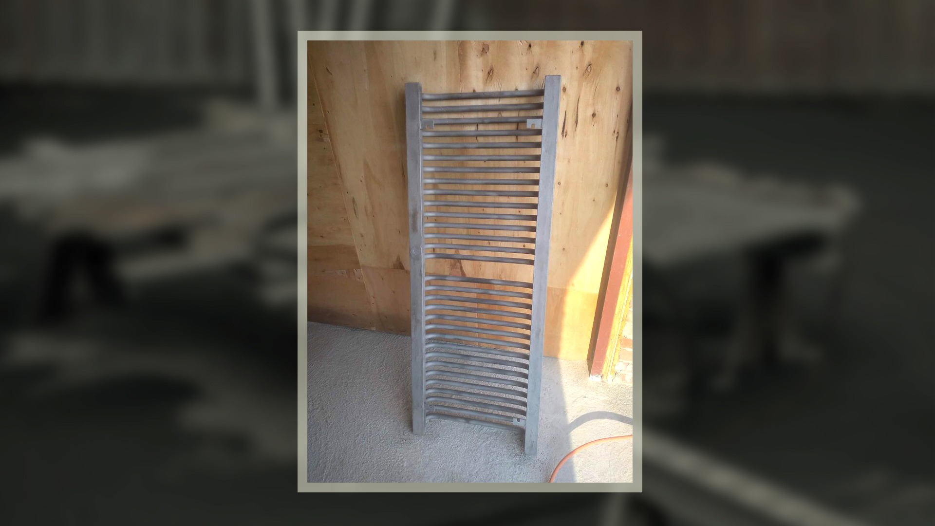 Metalowy grzejnik łazienkowy po piaskowaniu, widoczne ślady obróbki, surowe drewno w tle.