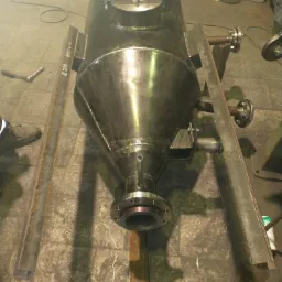 Metalowy zbiornik o stożkowym kształcie w trakcie produkcji, wsparty na metalowych profilach, widoczne spawy i elementy mocujące.