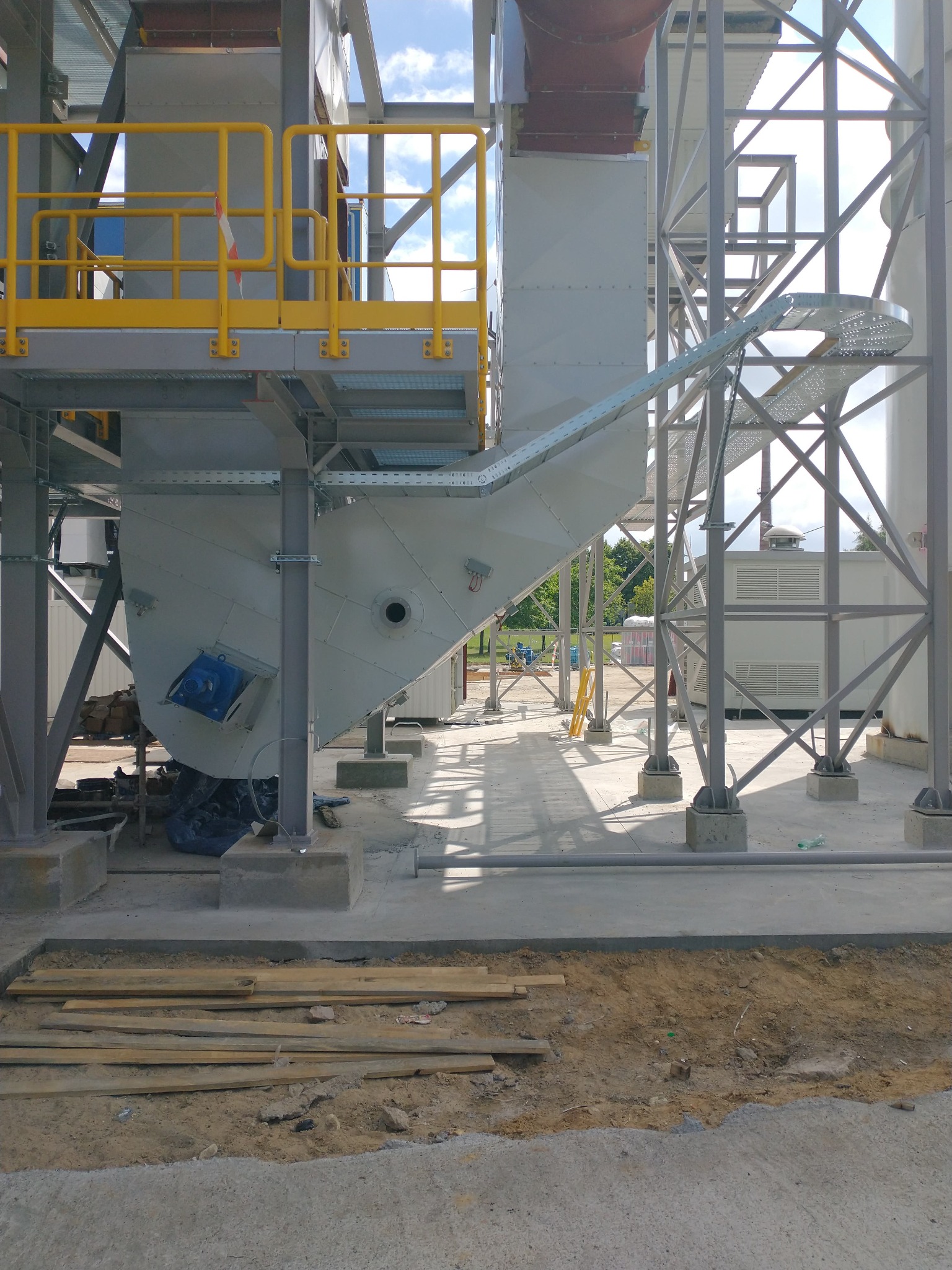 Konstrukcja hali przemysłowej w trakcie budowy: widok na metalową konstrukcję wsporczą, elementy transportu materiałów i fragment placu budowy.