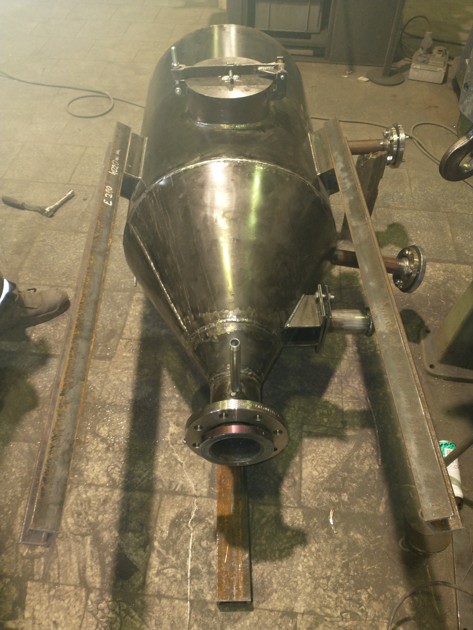 Metalowy zbiornik o stożkowym kształcie w trakcie produkcji, wsparty na metalowych profilach, widoczne spawy i elementy mocujące.