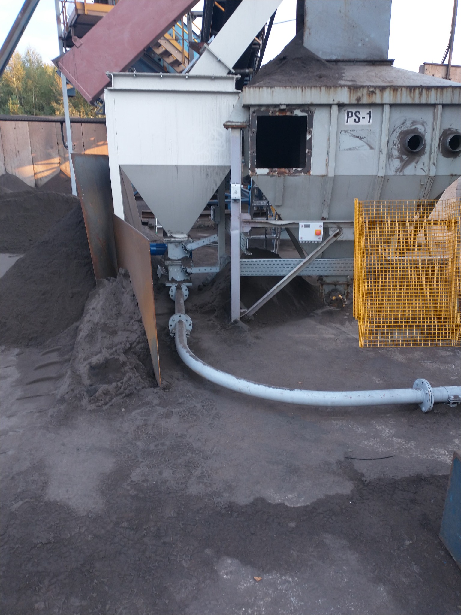 Konstrukcja stalowa PS-1 z lejowatym zbiornikiem wypełnionym szarym materiałem sypkim, połączona rurą z ziemią, zabezpieczona żółtą kratą.