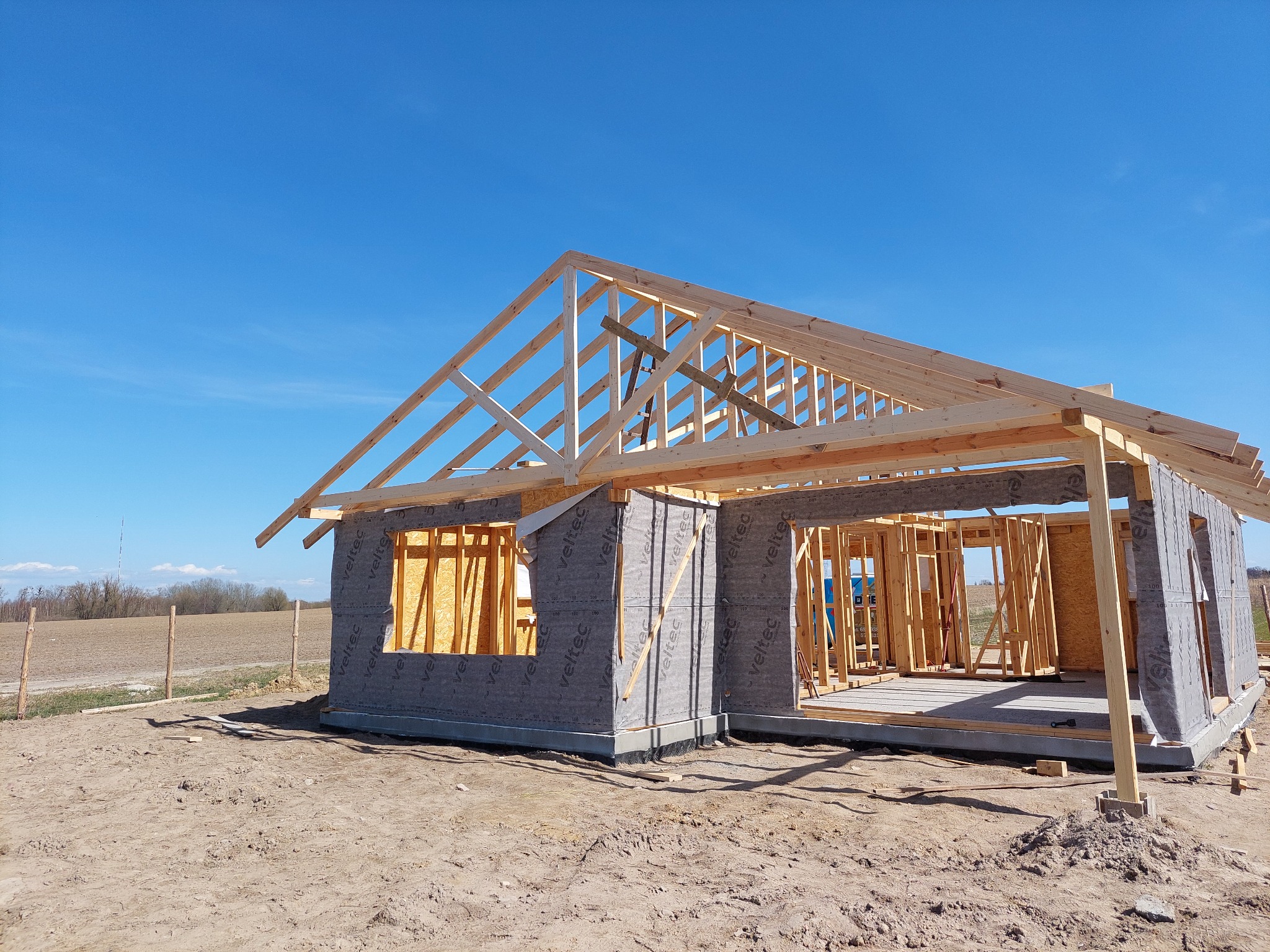 Budowa domu szkieletowego w Bydgoszczy, widoczna konstrukcja ścian z płyt OSB i izolacji oraz drewniany szkielet dachu na tle błękitnego nieba.