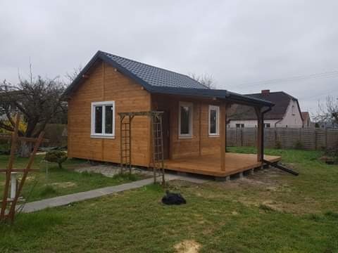 Gotowy, drewniany domek z zadaszonym tarasem, widoczny z zewnątrz w pochmurny dzień, z elementami dekoracyjnymi w postaci drabinki ogrodowej.