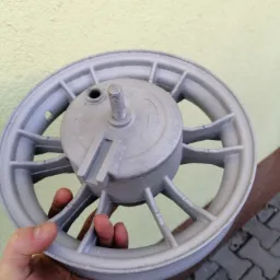 Szare, odnowione koło od skutera trzymane w dłoni na tle ściany i kostki brukowej.