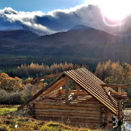 Wznoszenie surowego stanu domu z bali na tle górskiego krajobrazu z widocznym żurawiem budowlanym.