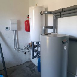 Nortmar Oddział Opole - Zestaw dwóch zbiorników akumulacyjnych w kotłowni, z szarym zbiornikiem Ferroli na pierwszym planie i białym zbiornikiem z czerwonym naczyniem wzbiorczym w tle, połączone rurami z izolacją.