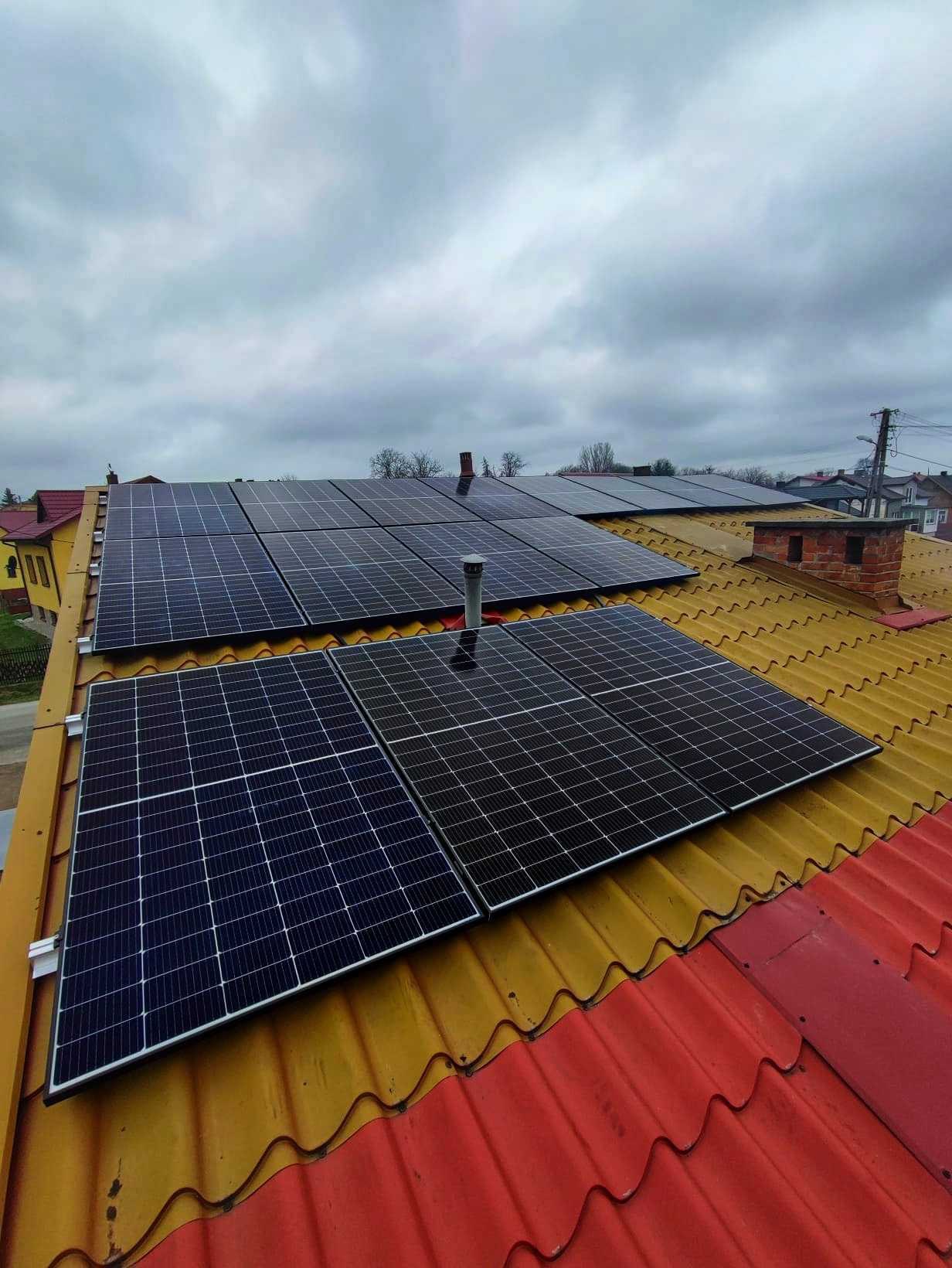 Panele słoneczne zamontowane na dachu domu z żółto-czerwoną dachówką w pochmurny dzień.