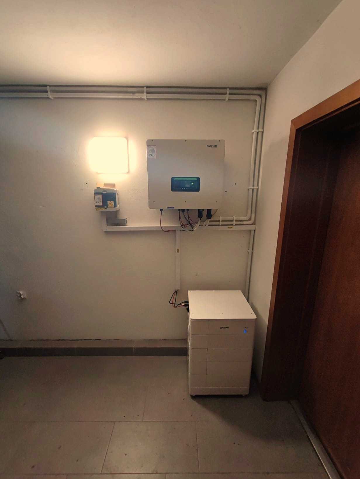 Biały inwerter fotowoltaiczny marki Sofar oraz moduł magazynu energii w jasnym pomieszczeniu z widoczną instalacją elektryczną.