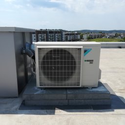 KlimaHome Sp. z o.o. - Jednostka zewnętrzna klimatyzatora Daikin zamontowana na betonowej podstawie na dachu budynku z widokiem na zabudowę miejską w tle.