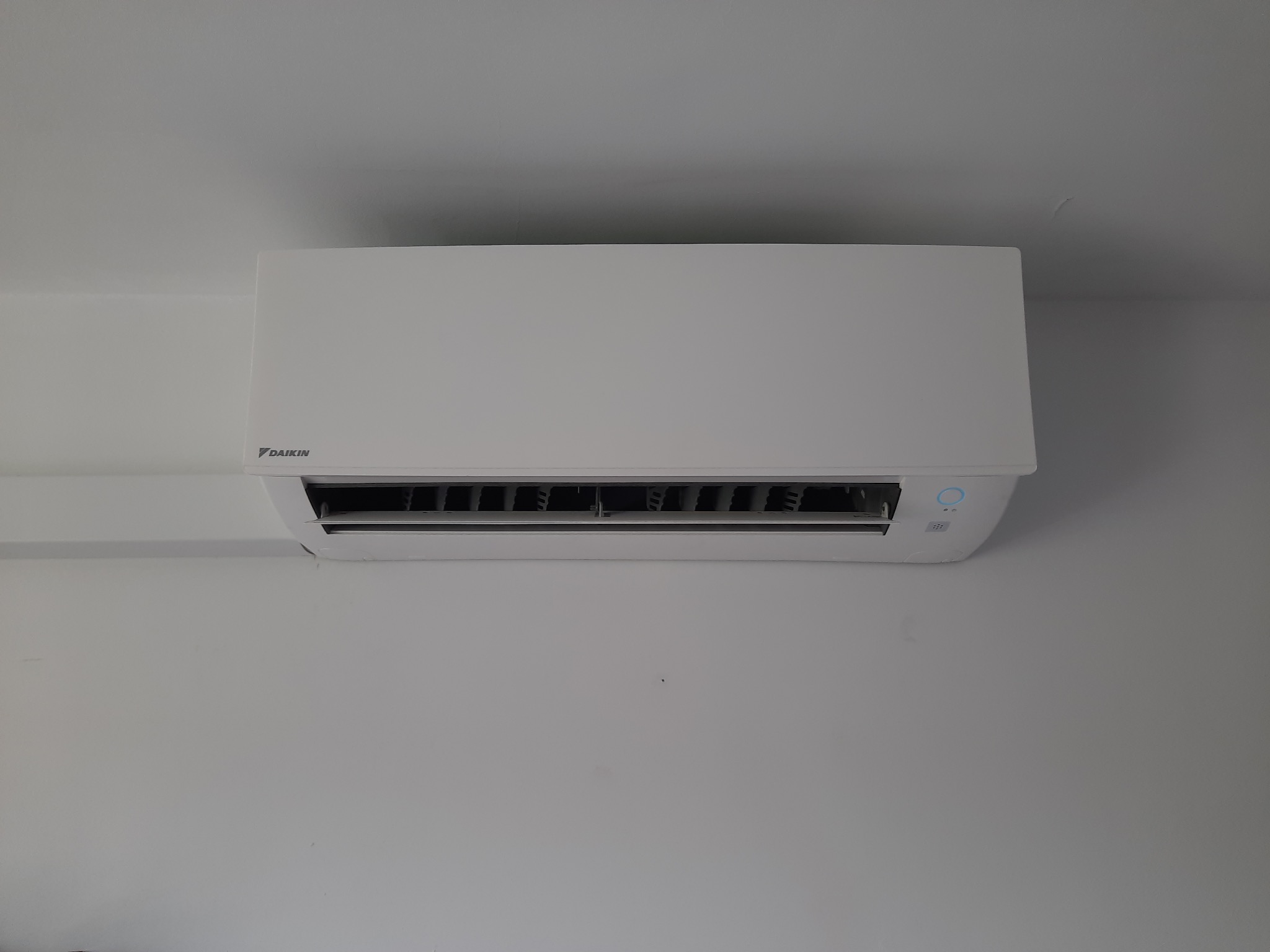 Biała jednostka wewnętrzna klimatyzatora Daikin zamontowana na białej ścianie, widok od dołu.