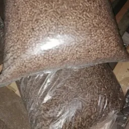 Dwa worki przezroczystego plastiku wypełnione brązowymi granulkami opału, jeden worek leży na drugim, widoczne drewniane deski w tle.