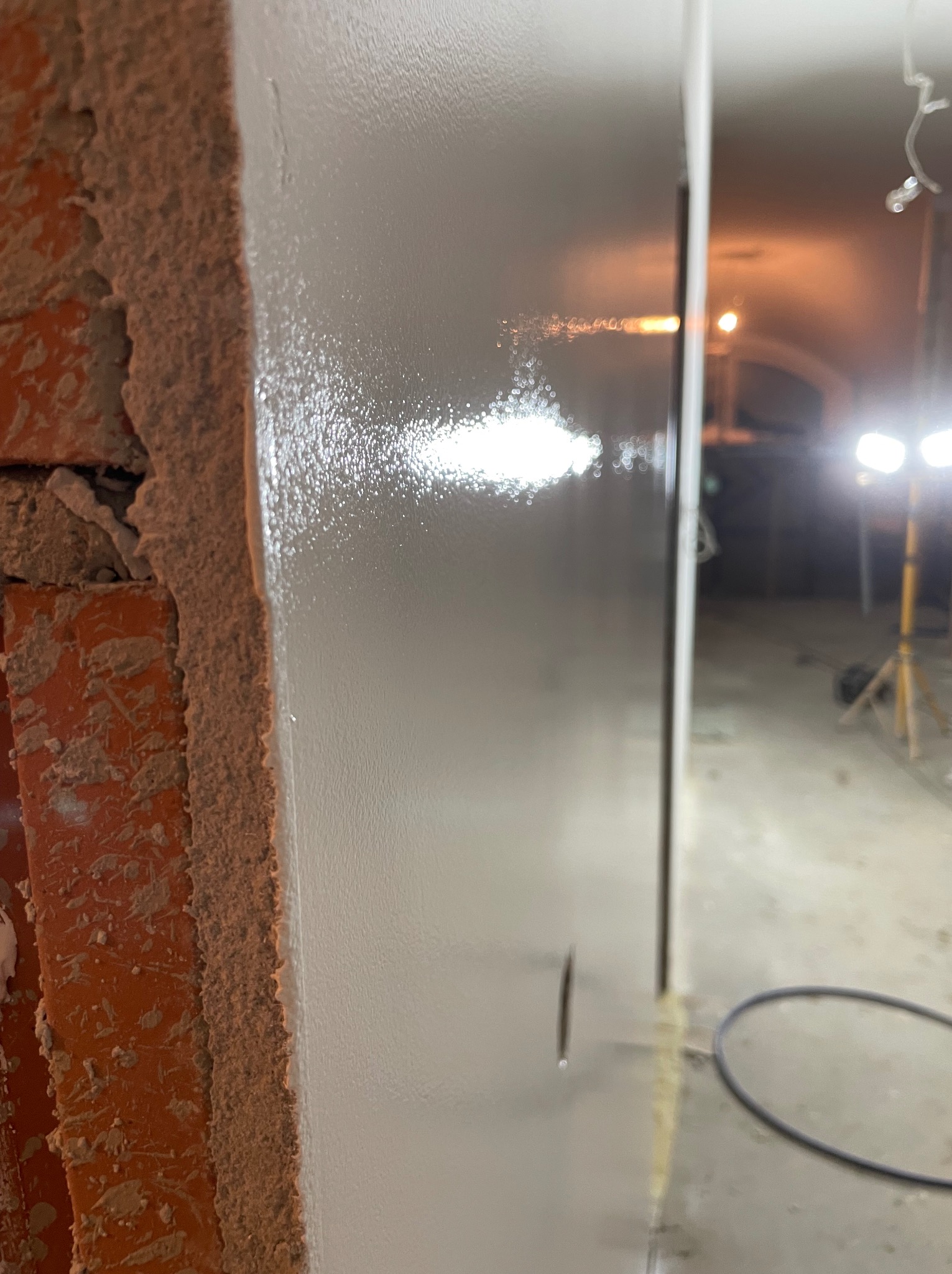 Gładź na ścianie z ceglanym fragmentem w Ostrzeszowie. Widoczne ślady po szpachlowaniu i niedoskonałości powierzchni, sugerujące etap prac wykończeniowych.