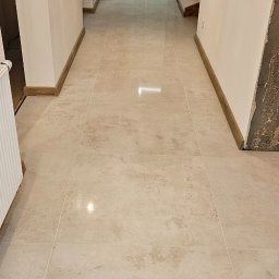 ProBau K&W - Beżowa, połyskująca podłoga z płytek w korytarzu z łukowatymi przejściami; widoczna łazienka w trakcie remontu.