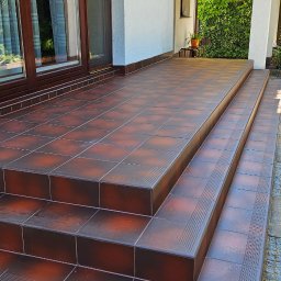 ProBau K&W - Brązowe płytki na schodach zewnętrznych prowadzących do domu. Widoczne detale wykończenia i fuga. Schody z płytek na zewnątrz budynku.