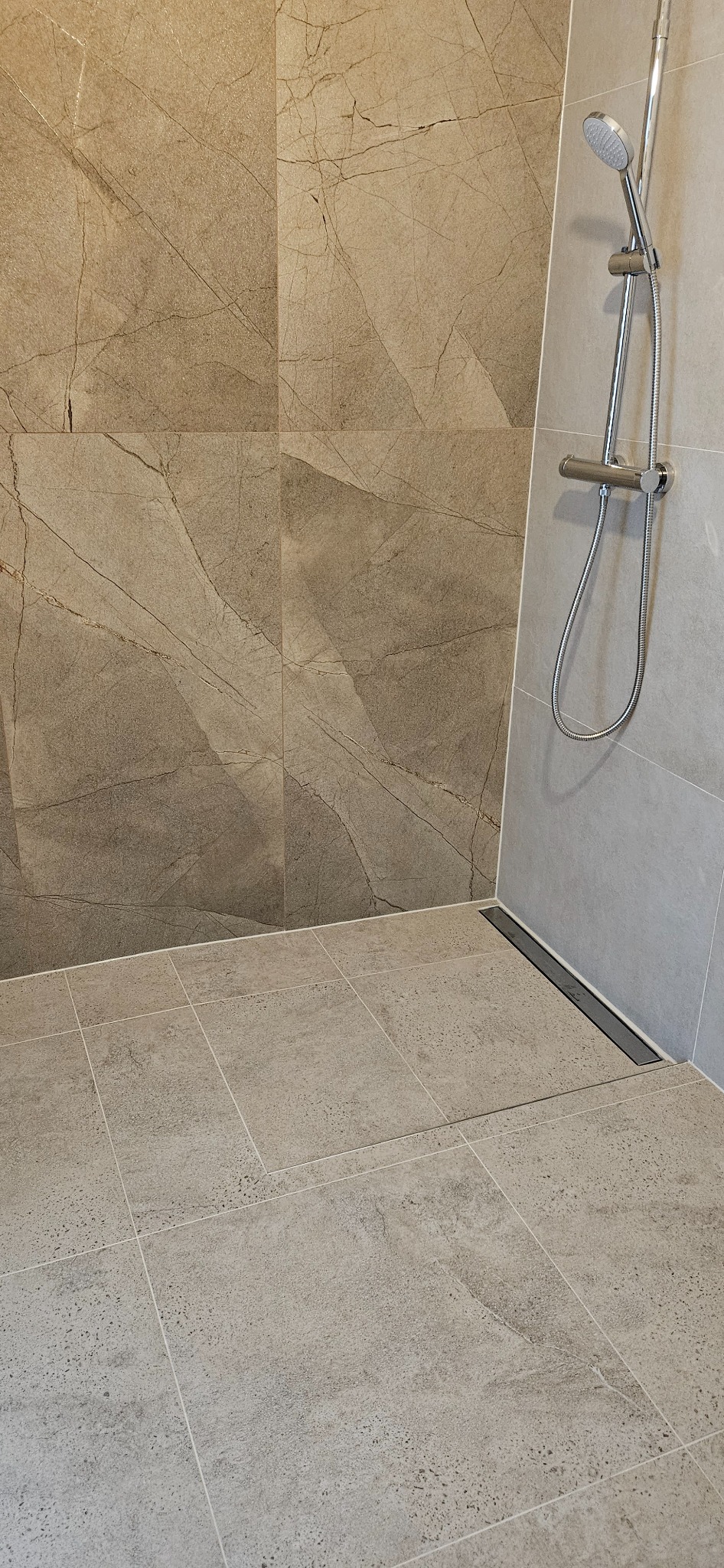 Wykończona kabina prysznicowa z odpływem liniowym i beżowymi płytkami imitującymi marmur na ścianach. Minimalistyczny design.