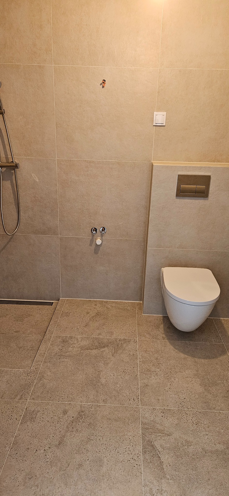 Beżowa łazienka po remoncie: wisząca toaleta, odpływ liniowy, armatura, płytki imitujące kamień na ścianach i podłodze. Ukończona realizacja.