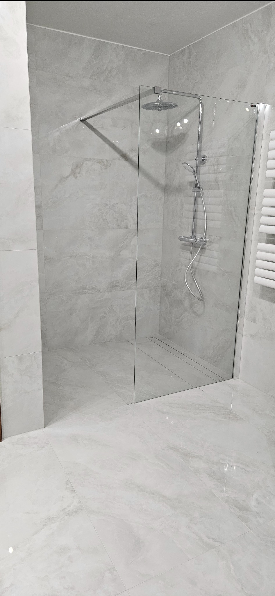 Nowoczesna kabina prysznicowa walk-in z deszczownicą i odpływem liniowym, wykończona płytkami imitującymi marmur w odcieniach szarości. Minimalistyczny design.