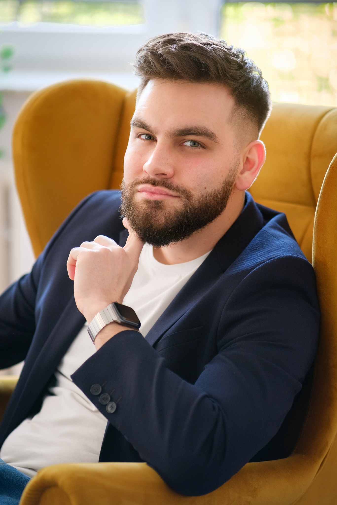 Portret mężczyzny w marynarce, siedzącego w złotym fotelu w Warszawie, z ręką pod brodą i zegarkiem na nadgarstku.