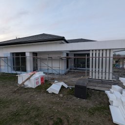 RP. Radosław Paździor - Dom w trakcie ocieplania elewacji, widoczne rusztowania i białe płyty izolacyjne. Częściowo ocieplone ściany i przygotowane materiały budowlane na posesji.