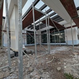 RP. Radosław Paździor - Dom w trakcie ocieplania elewacji styropianem, widoczne rusztowania i fragmenty materiału ociepleniowego na ziemi. Kolumny dekoracyjne na elewacji.