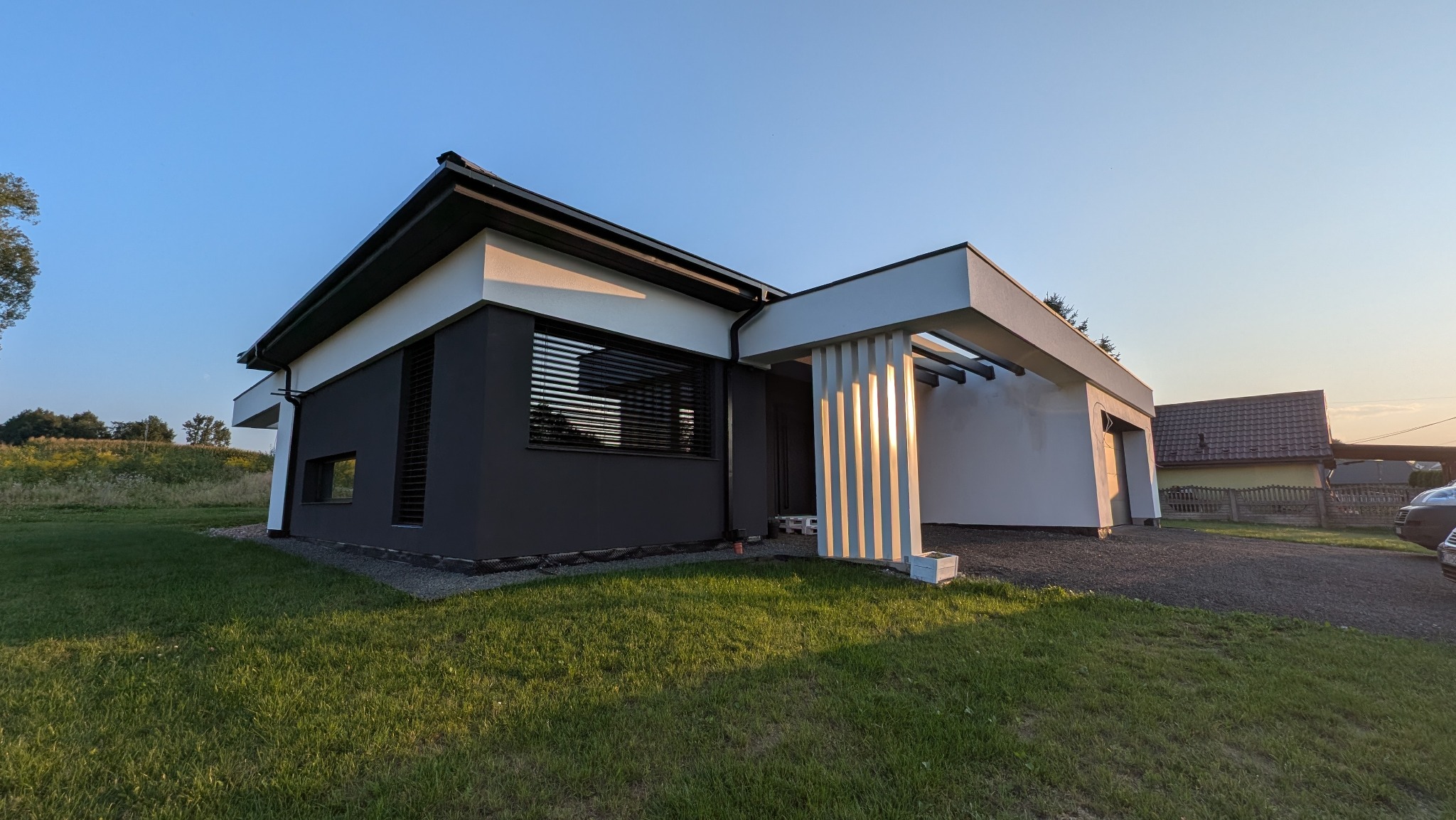 Nowoczesny dom jednorodzinny z płaskim dachem i elewacją w odcieniach szarości i bieli, z elementami dekoracyjnymi w postaci pionowych listew.