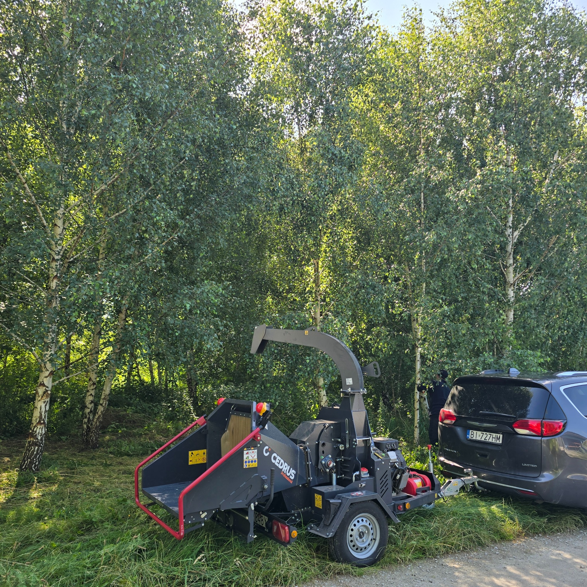 Rozdrabniacz do gałęzi Cedrus podłączony do samochodu na tle drzew. Sprzęt gotowy do pracy przy wycince drzew i pielęgnacji zieleni.
