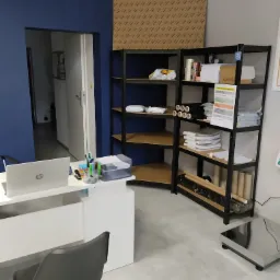 Biuro firmy transportowej: biurko z laptopem, regał z materiałami do pakowania, waga do paczek.