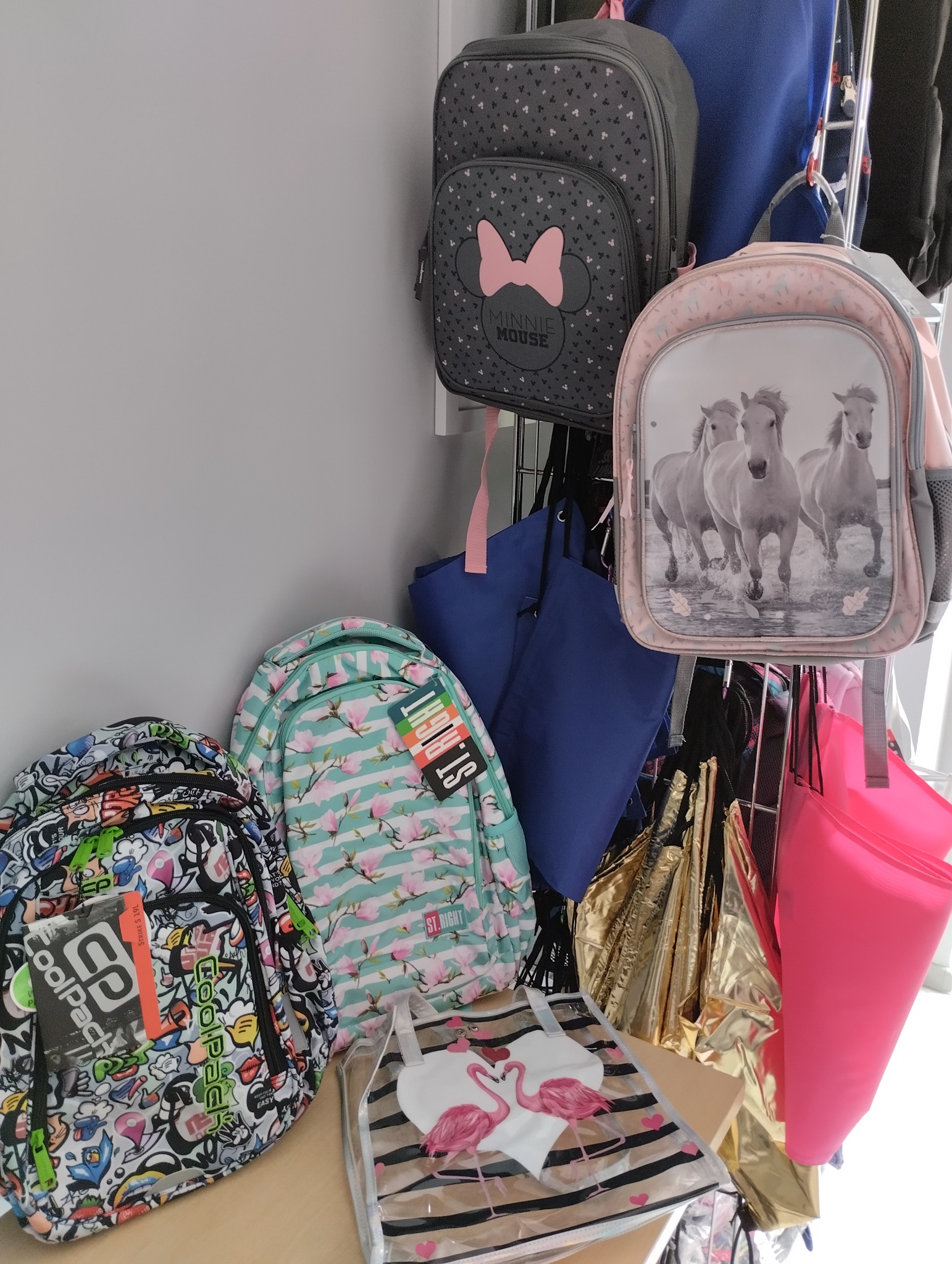Różnorodność plecaków i toreb wiszących na wieszaku: plecak z motywem Myszki Minnie, plecak z biegnącymi końmi, plecak w kwiaty magnolii marki St.Right, plecak z graffiti CoolPack...