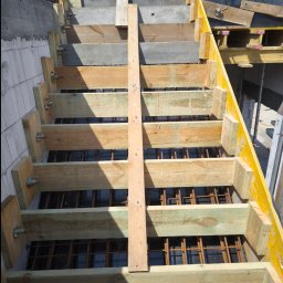 SBK-Instal - Szkielet schodów z desek i zbrojenia stalowego, widok z góry, konstrukcja szalunkowa z żółtymi elementami, przygotowanie do wylewki betonu.