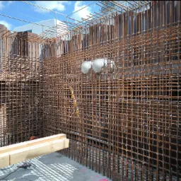 Siatka zbrojeniowa ułożona w wykopie, przygotowana do zalania betonem, widoczne metalowe szalunki i instalacja wentylacyjna, na pierwszym planie deski i narzędzia.