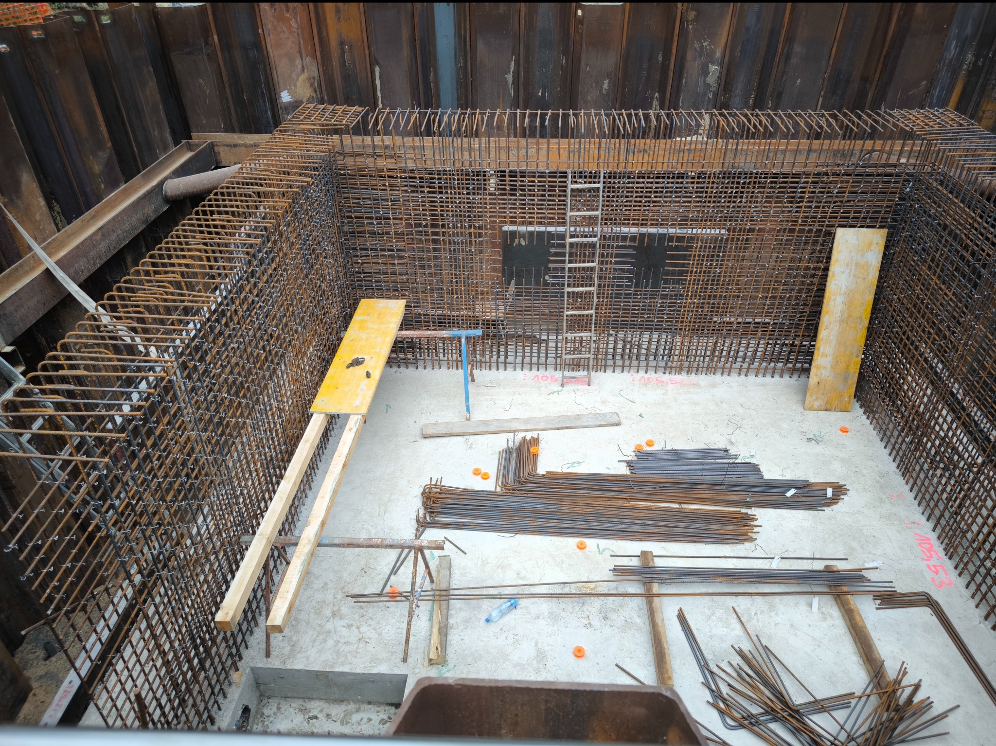 Siatka zbrojeniowa w wykopie, przygotowana do zalania betonem, widoczne elementy szalunkowe i stalowe profile zabezpieczające wykop.