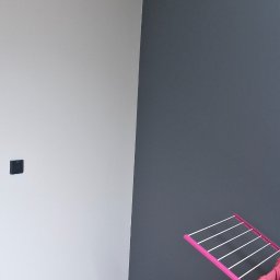 Ekipa Malarska - Świeżo pomalowane wnętrze z szarą ścianą, drewnianą podłogą i suszarką na ubrania. Widoczne gniazdka elektryczne i wystające kable od oświetlenia.