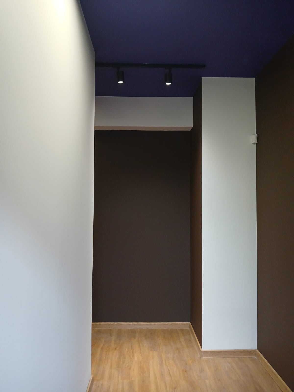 Pomieszczenie po malowaniu: białe i brązowe ściany, ciemnoniebieski sufit z oświetleniem punktowym. Podłoga wyłożona panelami w odcieniach drewna.