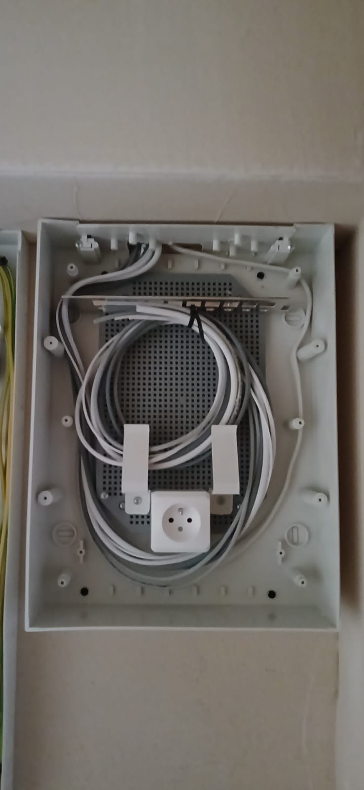 Otwarta skrzynka elektryczna z widocznymi kablami, gniazdkiem i elementami montażowymi. Widok z góry na instalację wewnątrz skrzynki.