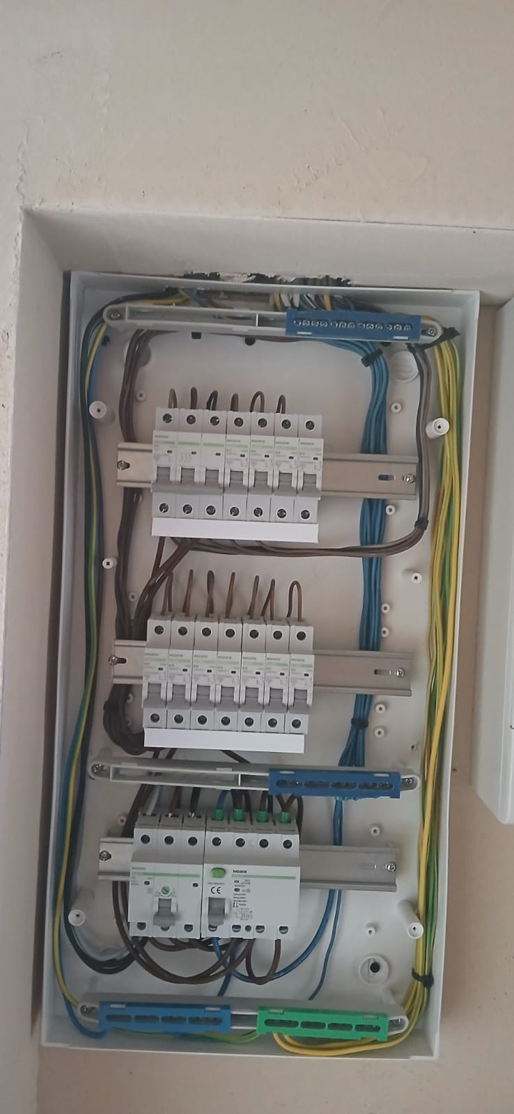 Rozdzielnia elektryczna w białej obudowie, widok z góry. Widoczne bezpieczniki, przewody w różnych kolorach i listwy zaciskowe. Instalacja schludna, gotowa do użytku.