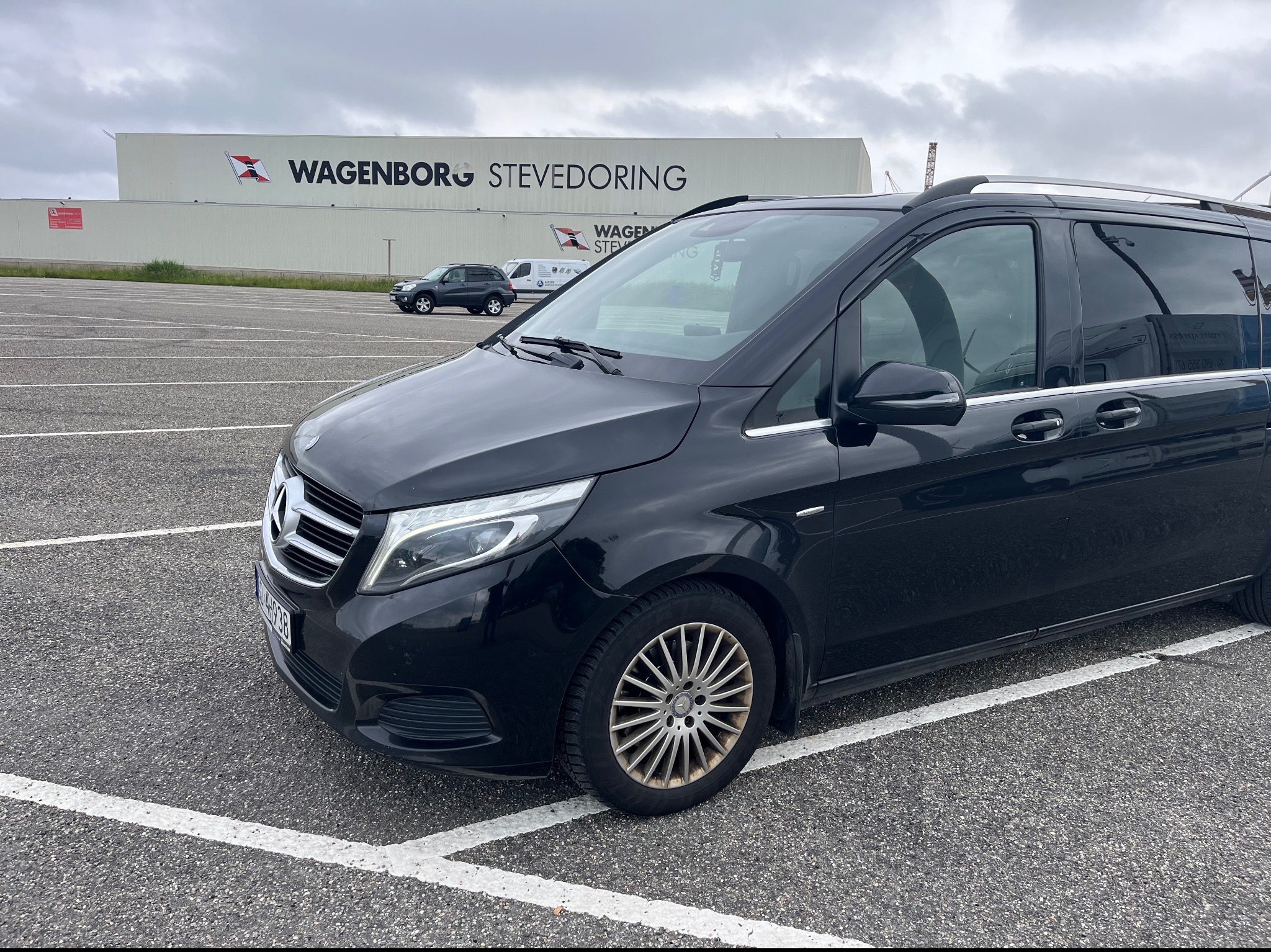 Czarny Mercedes-Benz V-klasy zaparkowany na parkingu, w tle budynek z napisem Wagenborg Stevedoring.