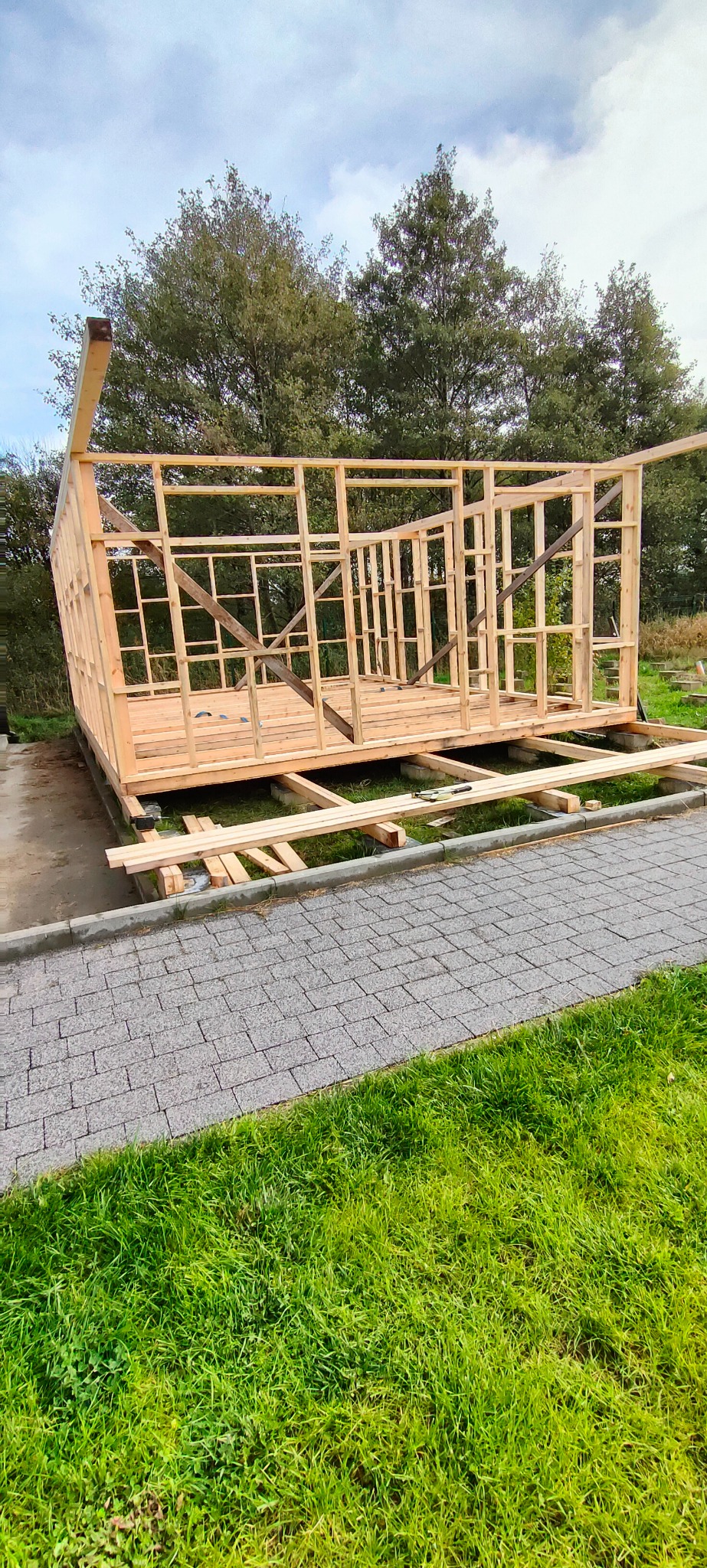 Konstrukcja szkieletowa drewnianej altany lub domku letniskowego w trakcie budowy, widok z zewnątrz na tle zieleni.