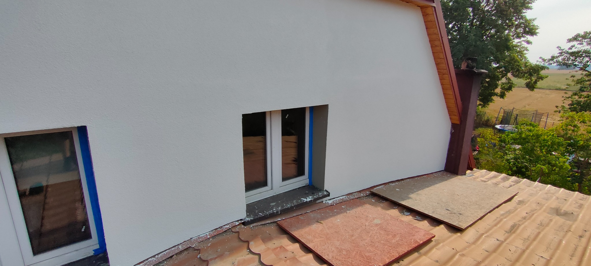 Ocieplony dom z nową, białą elewacją i zamaskowanymi oknami, widok z dachu podczas prac wykończeniowych.